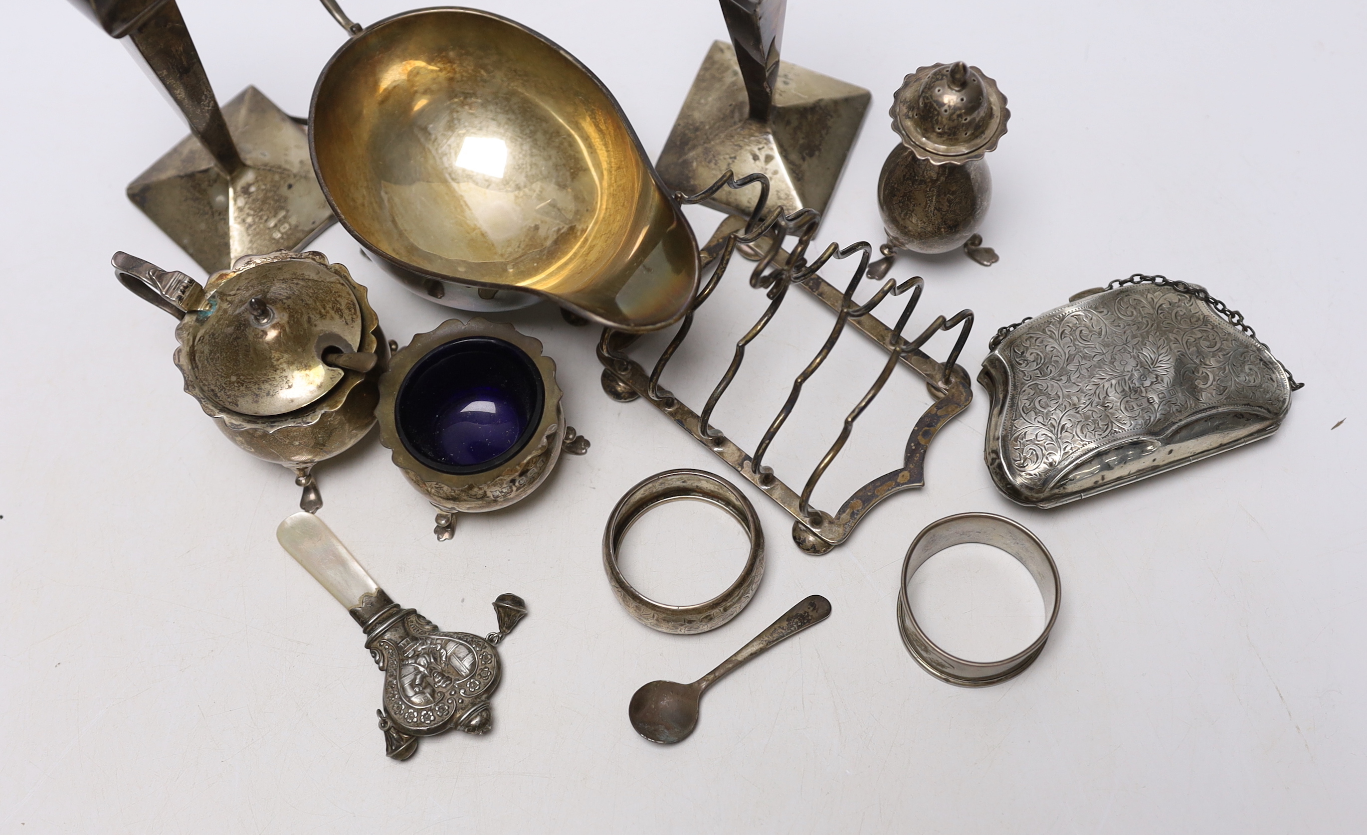 Sundry small silver including an Edwardian silver sauceboat, Birmingham, 1906, pair of spill vases (a.f.), a five bar toastrack, three condiments, a purse, two napkin rings and a child's rattle.
